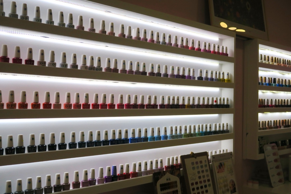 Quatre étagères rétroéclairées présentant des rangées de flacons de vernis OPI classés du rose au bleu nuit