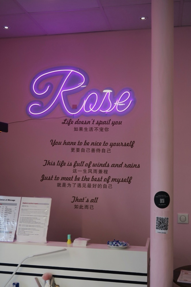 Néon rose en forme de mot « Rose » sur le mur du salon, au-dessus d’un poème calligraphié en français et en chinois