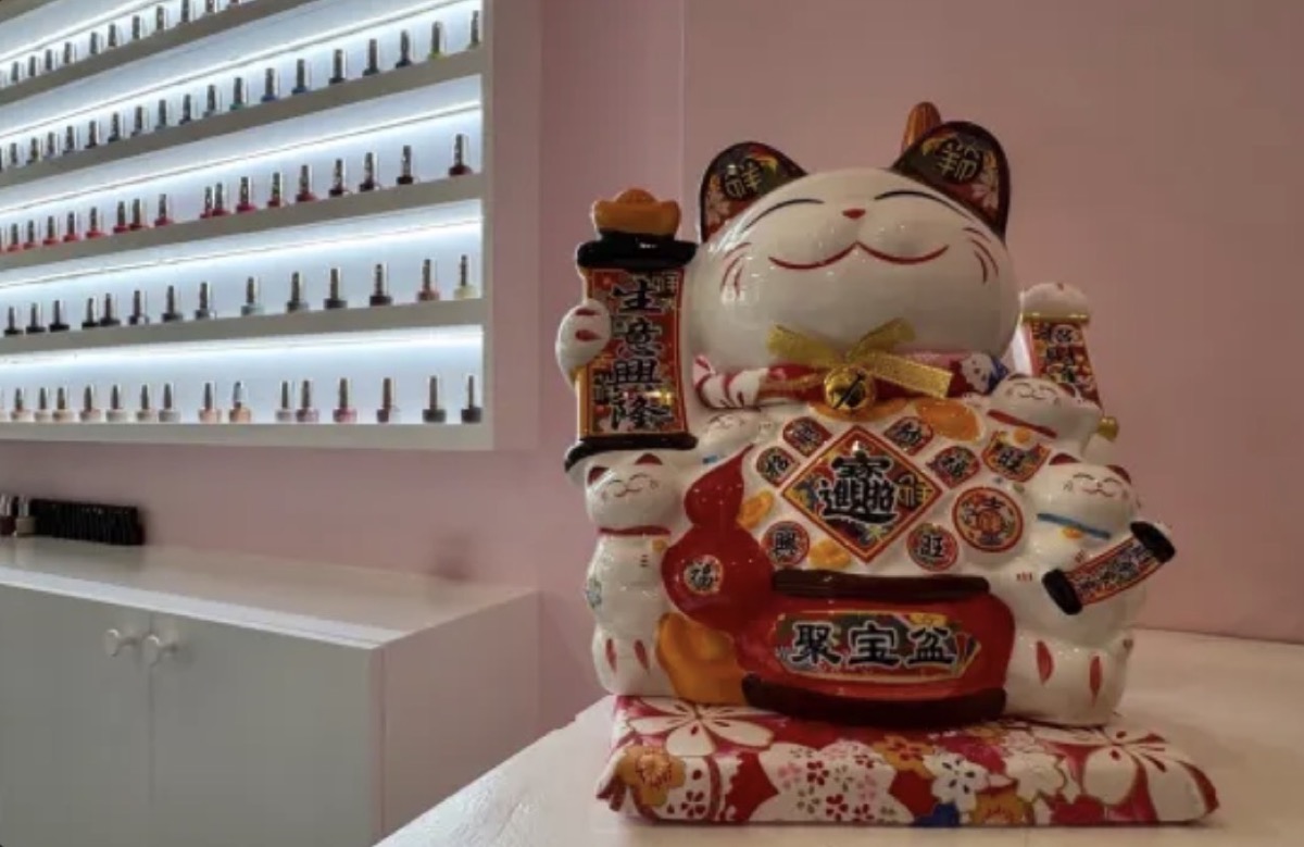 Chat porte-bonheur en céramique posé sur le comptoir du salon, devant le mur de vernis rétroéclairé et les murs roses