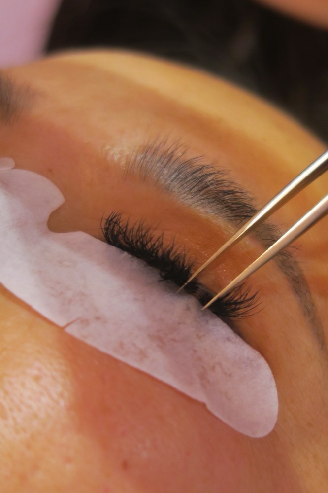 Pose d’extensions de cils à la pince, cil à cil, sur une cliente allongée