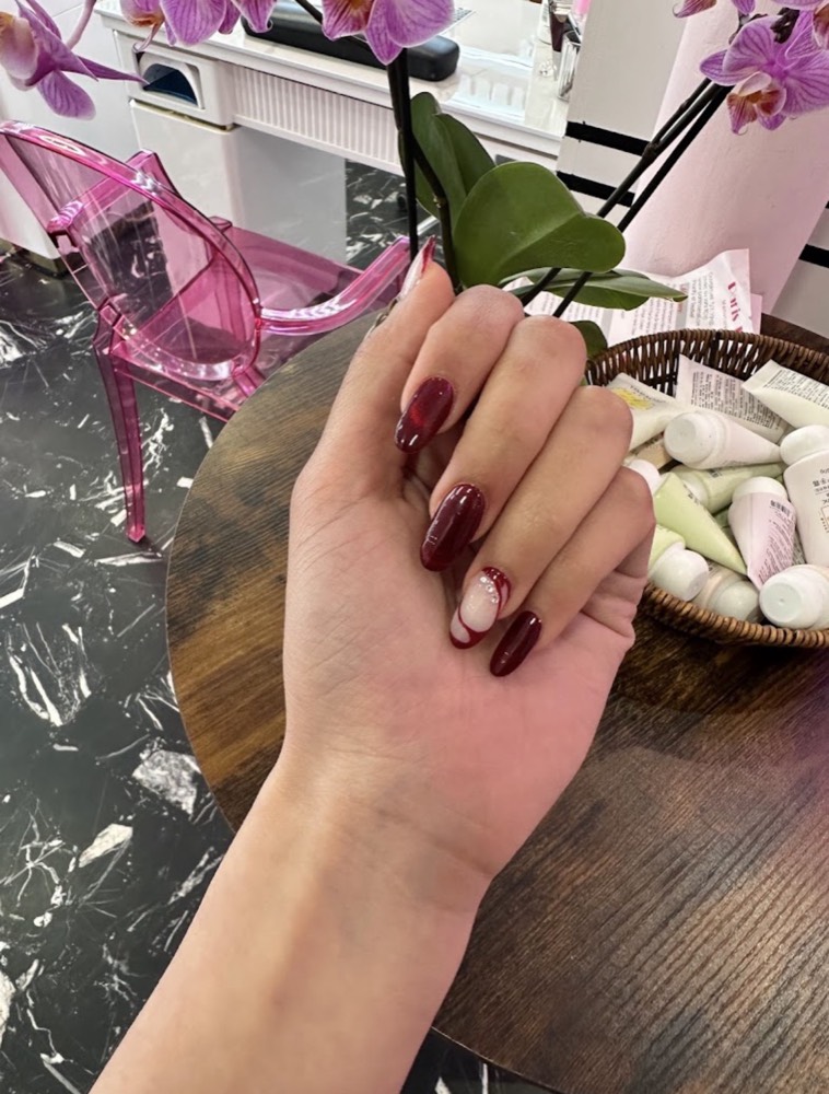 Main aux ongles longs en amande vernis bordeaux brillant, posée près d’une orchidée dans le salon