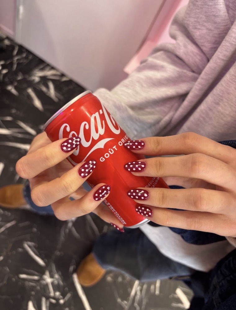 Mains aux ongles bordeaux ornés de pois blancs peints à la main, tenant une canette