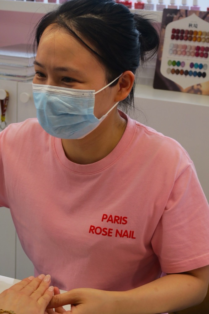 Prothésiste ongulaire de Paris Rose Nails en t-shirt rose du salon, concentrée sur une pose
